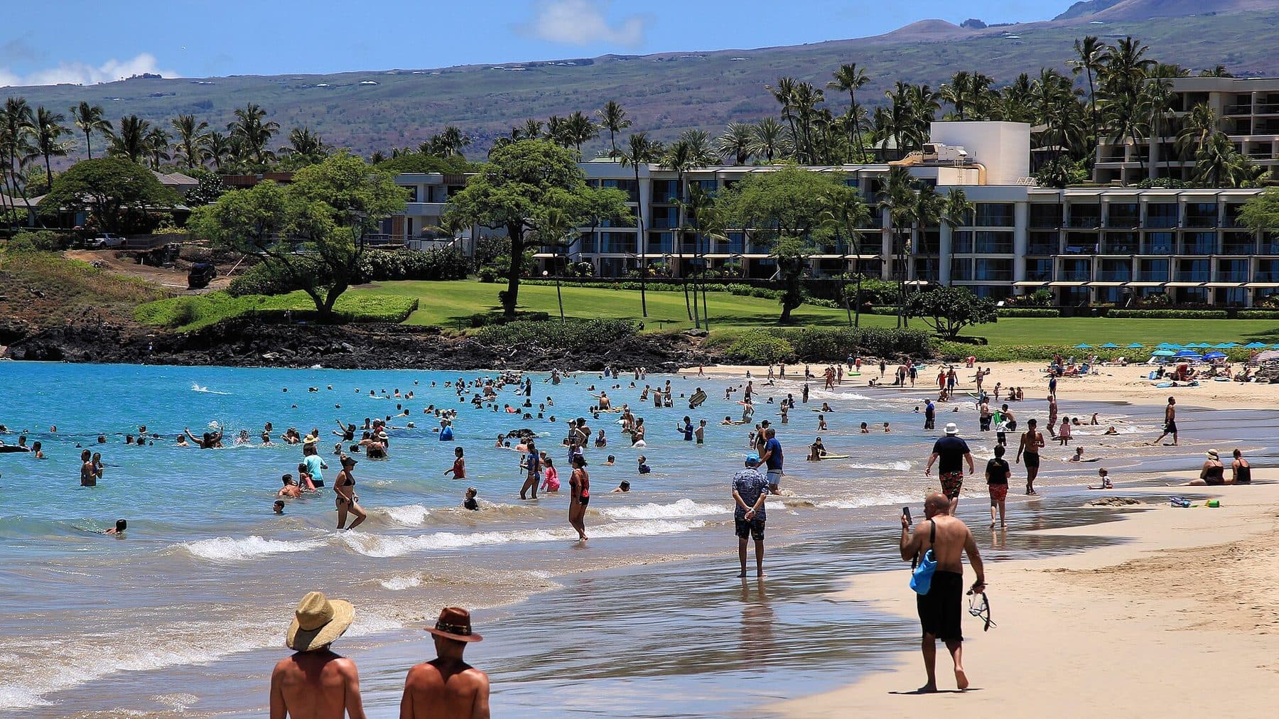 Swimmers and sunbathers at Hāpuna Beach, with a resort hotel and Kohala’s slopes behind