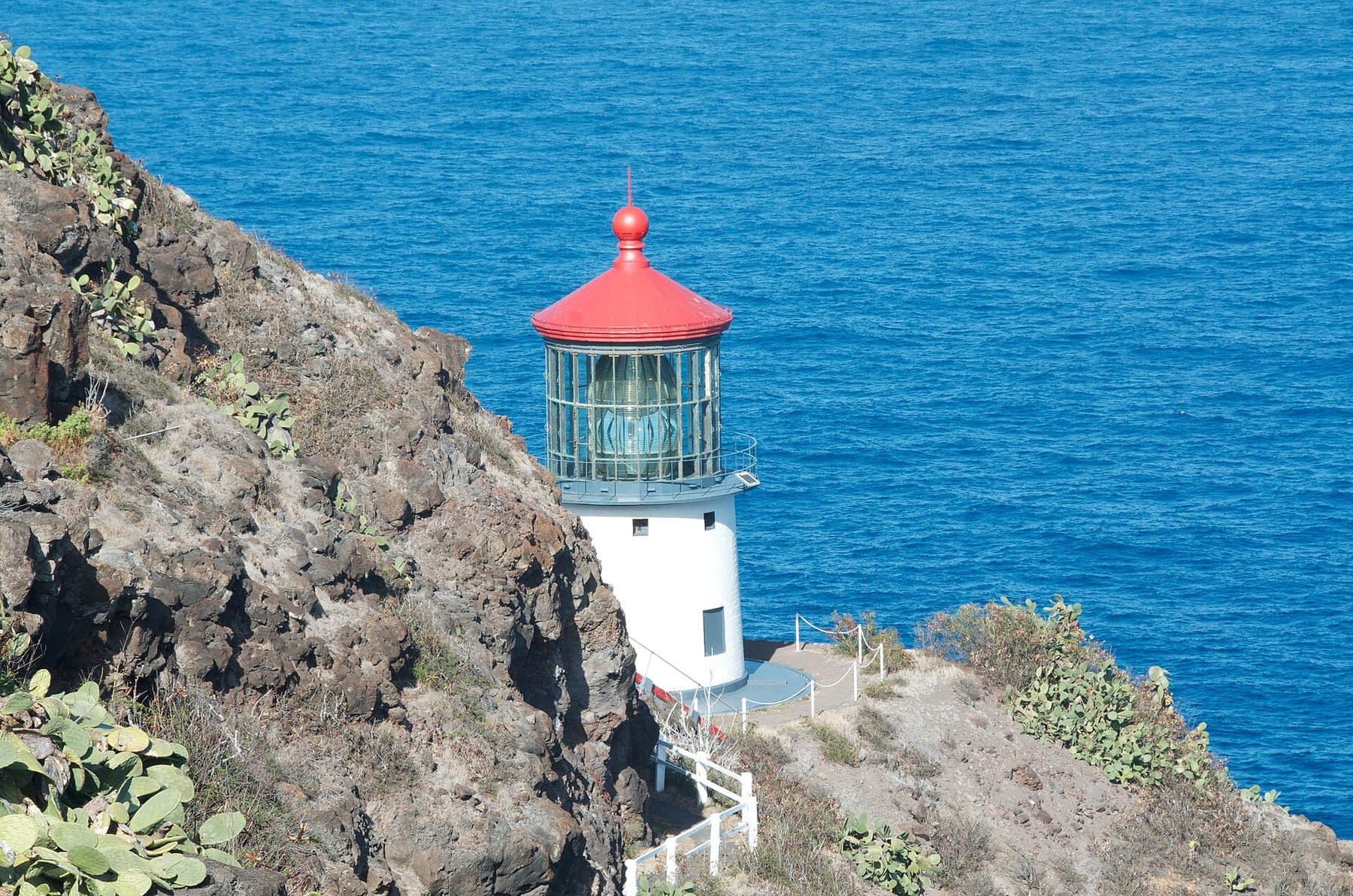 Red-roofed Makapuʻu Point Lighthouse on the sea cliff below the trail