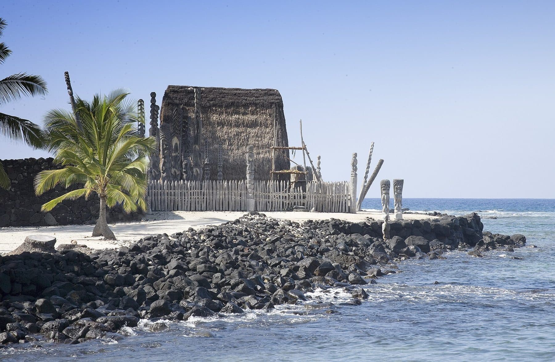 The thatched Hale o Keawe temple and carved kiʻi beside the sea at Puʻuhonua o Hōnaunau