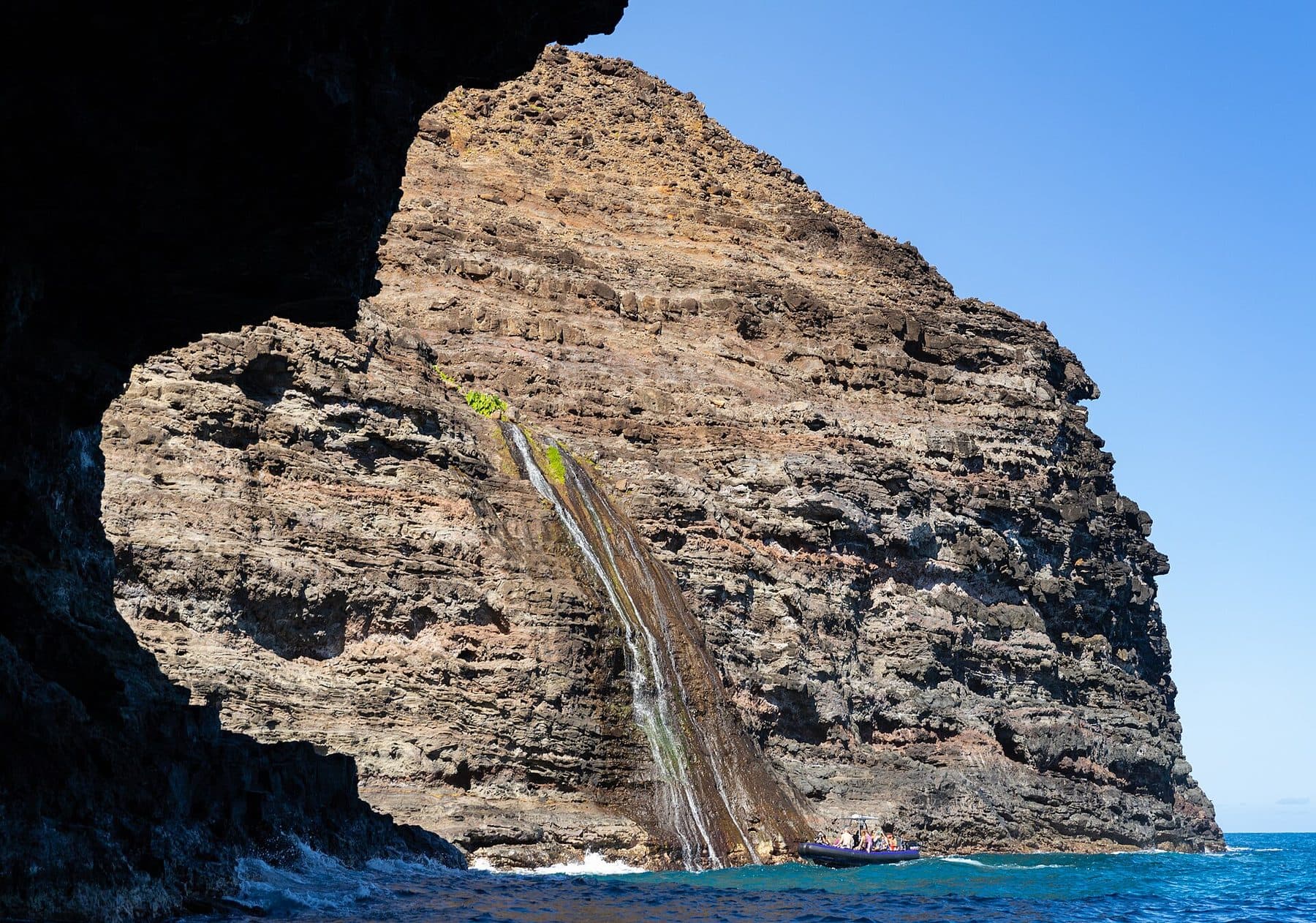 A waterfall pouring down the sea cliffs of the Nā Pali Coast on Kauaʻi