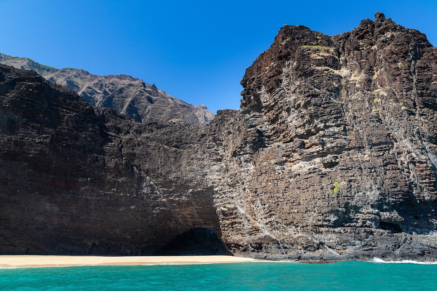 Sea cliffs and a sea cave above a small beach on the Nā Pali Coast