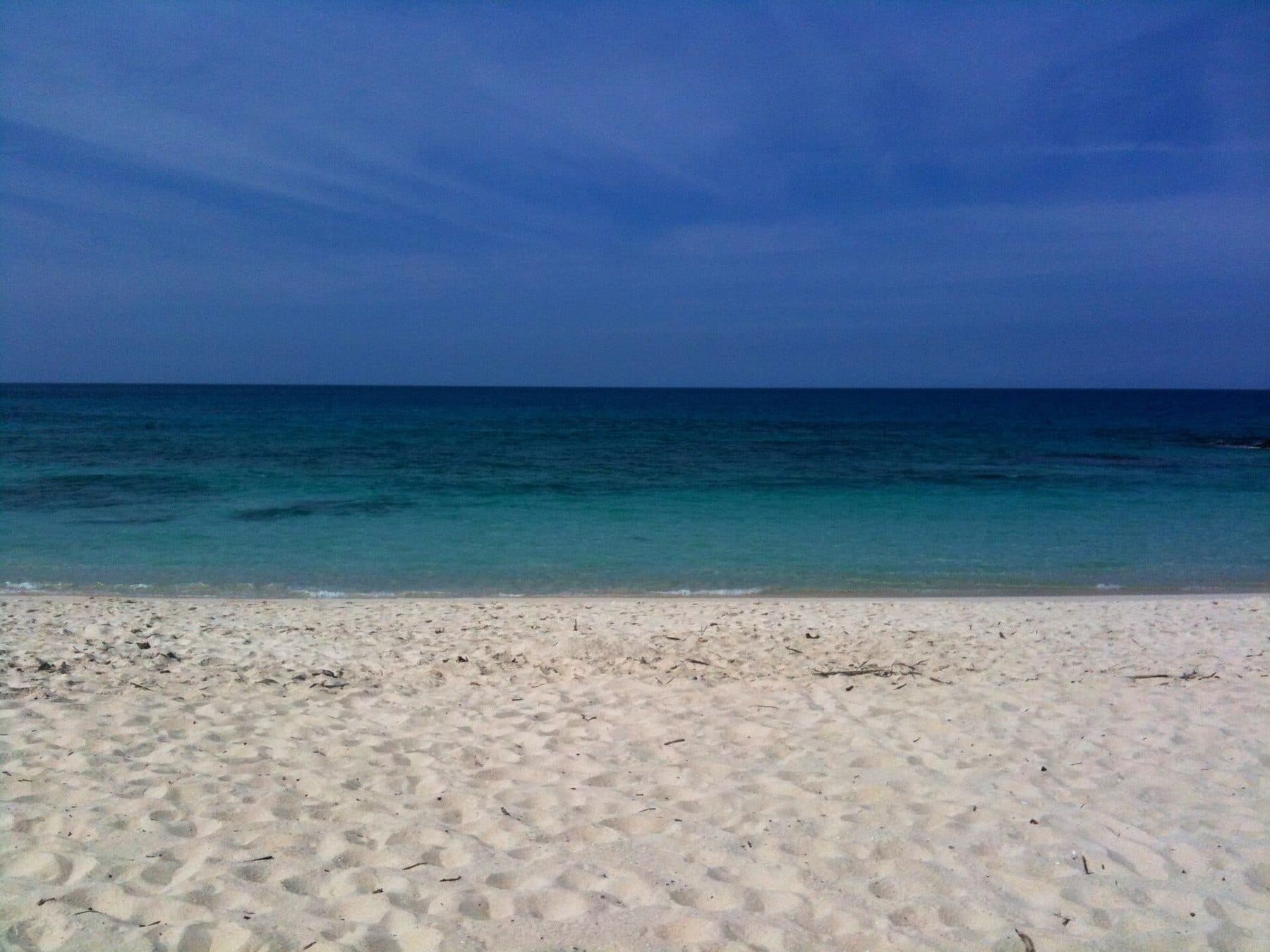 Empty white sand meeting deep blue water at Makalawena Beach